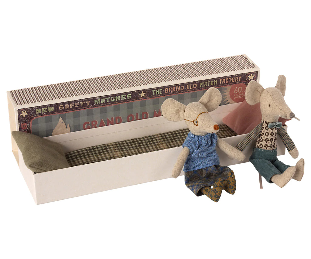 Two Maileg Grandma & Grandpa Mice in Matchbox dressed in colorful cotton clothes, seated inside an open matchbox labeled "the grand old match factory." One mouse wears a blue sweater, the other in green.