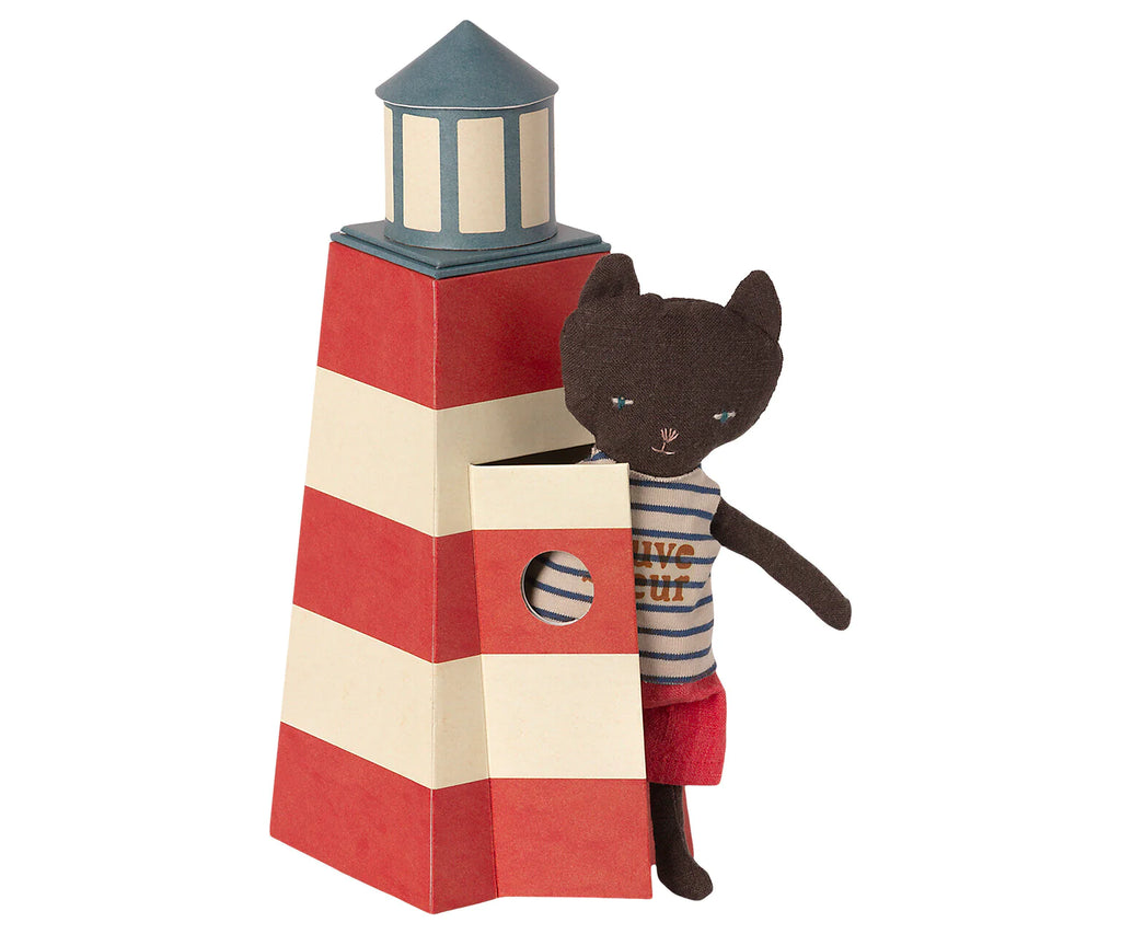 A Maileg Cat in Tower stands beside a red and white striped toy lighthouse with a small round window, peeking out as if on lifeguard duty, ready to watch over swimmers.