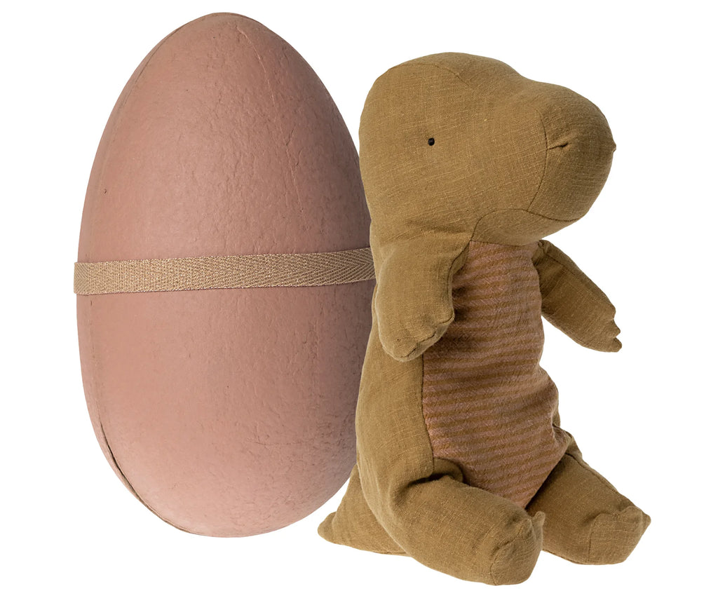 A Maileg Medium Gantosaurus in egg - Dark Ocher next to a large pastel pink egg with a ribbon around it, isolated on a white background.