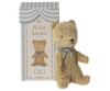 Image of a stuffed teddy bear next to a decorative box. The box's header reads "Maileg My First Teddy, Sand" and features an image of the bear adorned with a small gray ribbon around its neck. This classic baby keepsake comes in a striped blue and white top, perfect as a new born baby gift.