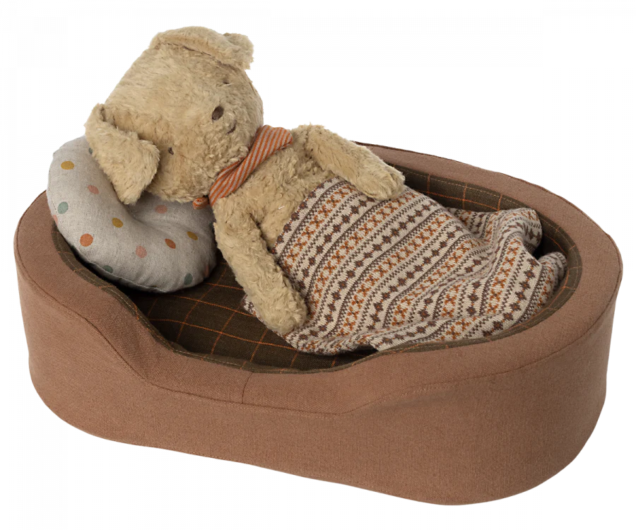 A toy dog bed with a toy dog laying in the bed with a pillow and a blanket.