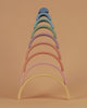 A colorful Raduga Grez 9-piece rainbow stacker consisting of arches in various pastel colors arranged in size order against a pale orange background.