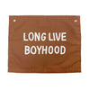 Long live boyhood in rust color photographed against white wall. 