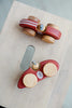 Two Handmade Wooden Toy Race Cars sit on a light-colored wooden surface. The toy car on the left has red stripes, while the one on the right is red with a white number "1" on the side. Made from sustainably harvested birch wood, both cars have round wooden wheels and small wooden drivers with hats.