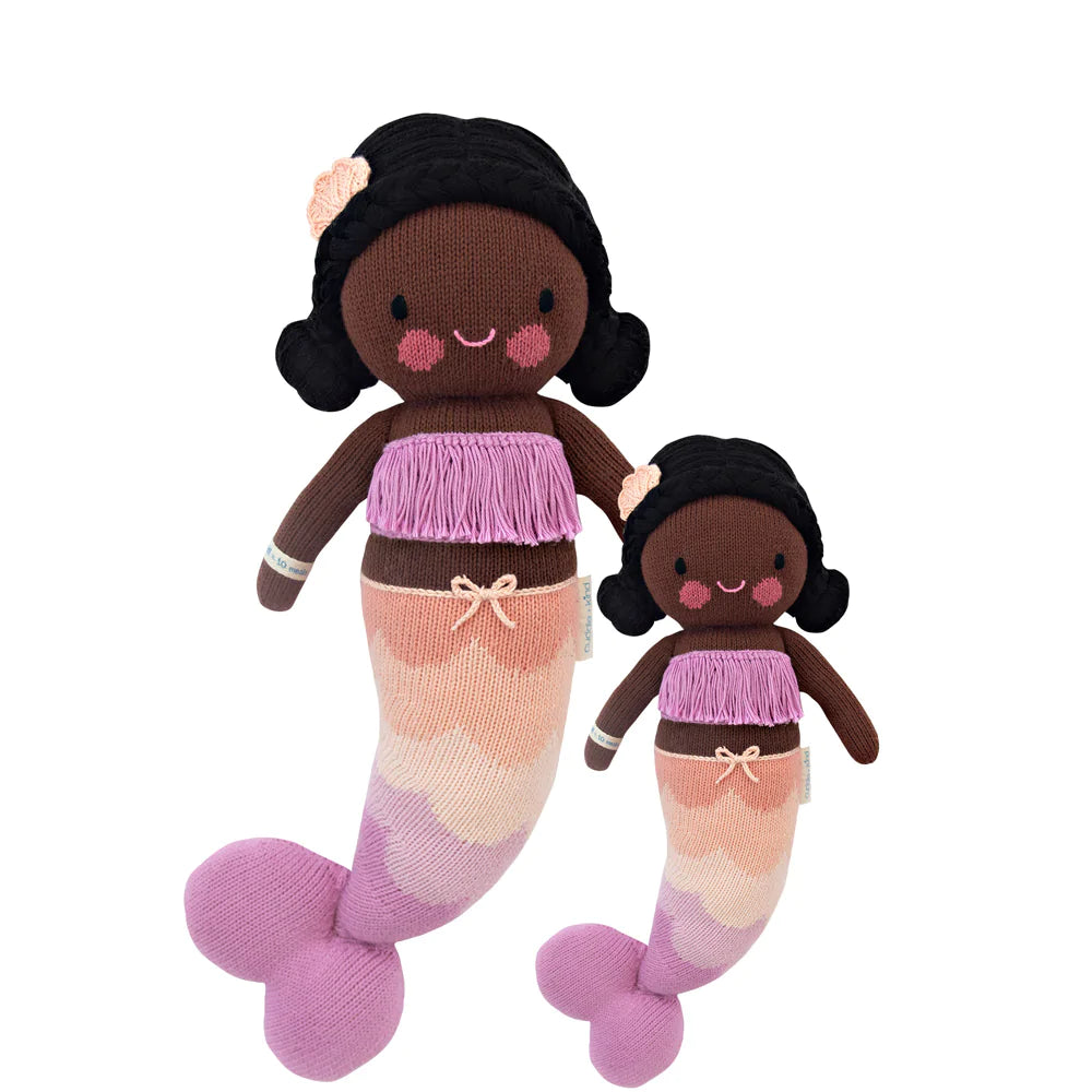 Two Cuddle + Kind Maya the Mermaid dolls with dark brown skin; one large and one small, both feature pink and white tails, purple tops, and smiling faces with rosy cheeks. They are filled with hypoallergenic cotton.