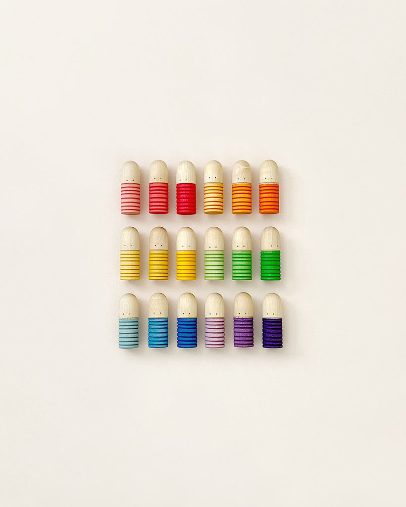 Four rows of colorful, wooden egg-shaped Grapat Buds/Brots toys, arranged neatly on a pale background. Each row contains eggs with the same colored horizontal stripes.