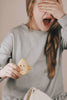 A person with long, light brown hair in a braid covers their eyes with one hand and holds a Wooden Ghost Emotions figure in the other. They are wearing a gray long-sleeve shirt and appear to be experiencing basic emotions of surprise or fear.