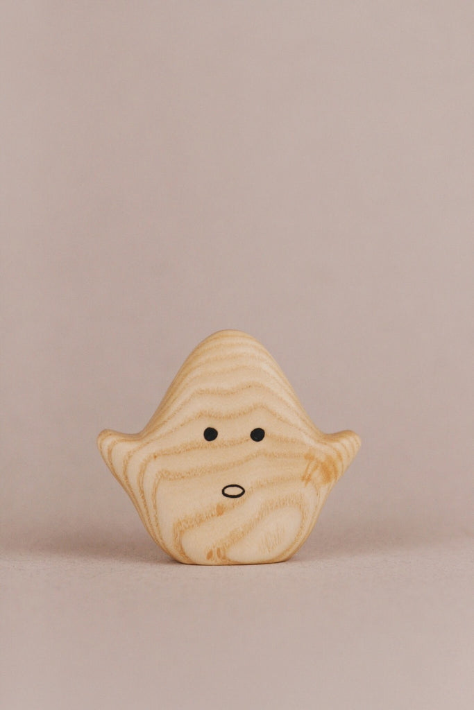 A small wooden toy shaped like a simplified ghost, finished with natural linseed oil to enhance the light wood grain. The Wooden Ghost Emotions, one of our charming wooden ghost figures, has black dot eyes and an open oval mouth expressing basic emotions, with its "arms" slightly raised against a soft beige background.