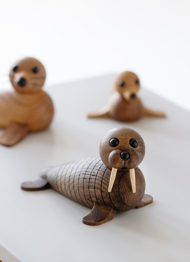 Three Spring Copenhagen Wally seal figurines on a white surface; the closest one is lying down with detailed engravings and small tusks, while the others are sitting up in the background. These handmade Spring Copenhagen Wally products.