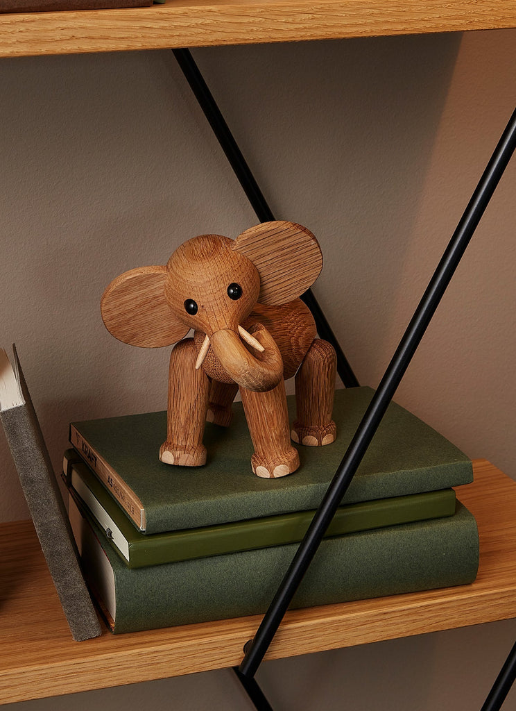 A Spring Copenhagen Ollie - Elephant figurine crafted from FSC Oak with large ears and a trunk sits on a stack of green books on a shelf.