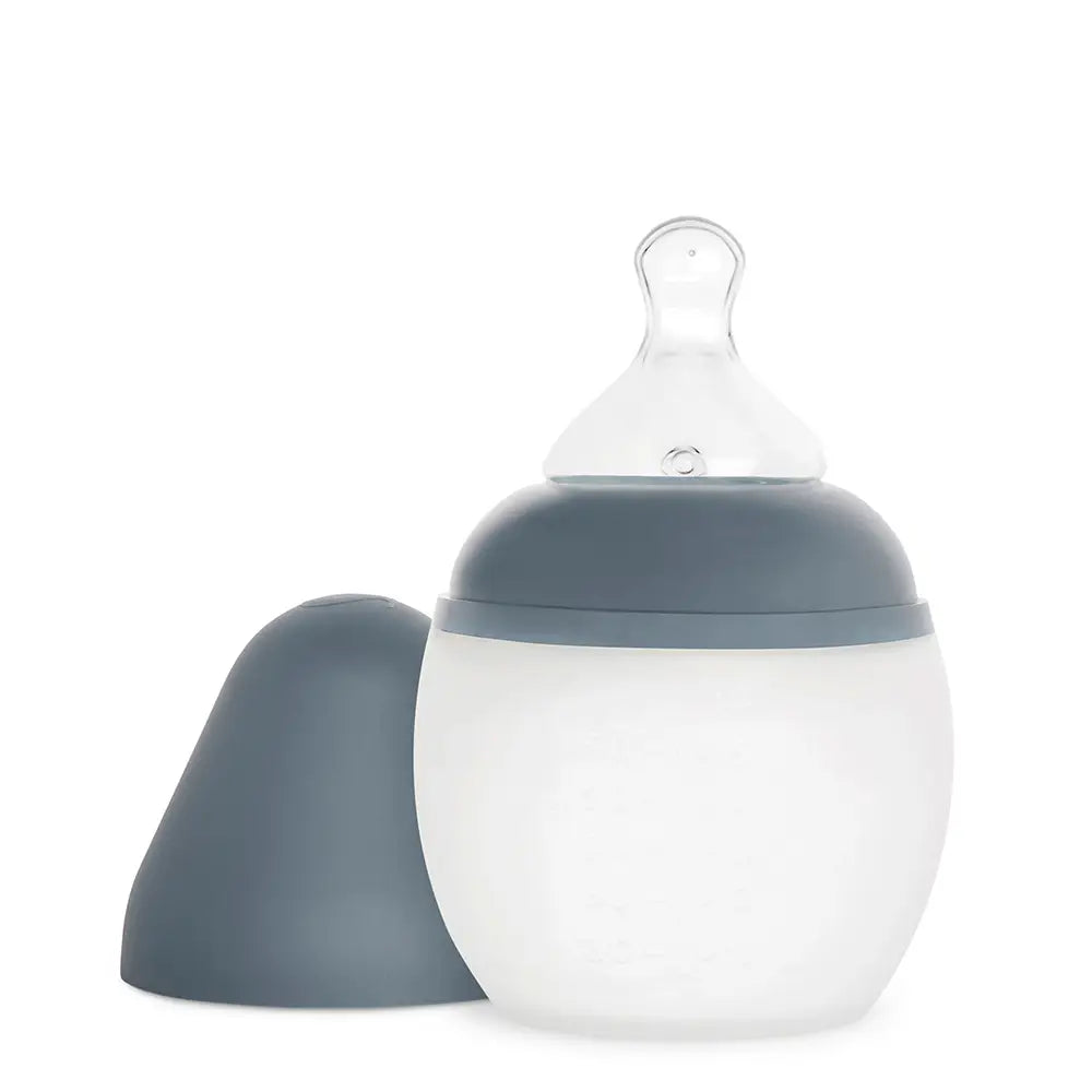 A Medical Grade Silicone baby bottle with a transparent, silicone nipple and a white and gray body, shown with its matching gray cap removed and placed beside it, against a white background.