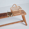 Pretend play natural color rattan shopping basket sitting wooden chair and white flowers laying next to it. Light gray background. 