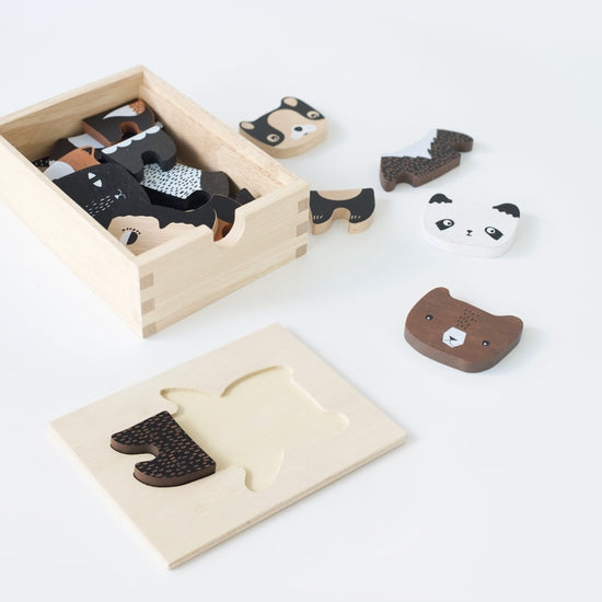 Mix & Match Animal Tiles shaped like animal faces, with a panda, bear, and fox, are scattered next to their corresponding slots in a wooden tray on a white surface. These creative play toys offer both