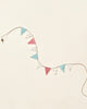 A decorative Maileg Miniature Garland of triangular bunting with alternating blue, pink, and polka-dotted flags against a pale beige background, perfect for child's room decor.