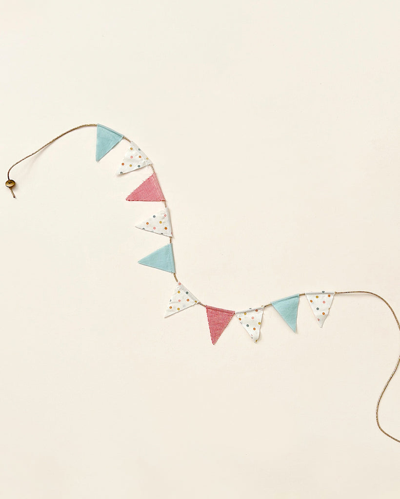 A decorative Maileg Miniature Garland of triangular bunting with alternating blue, pink, and polka-dotted flags against a pale beige background, perfect for child's room decor.