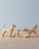 The Handmade Wooden Dog Family features three small ash wood dog figures—two adults and a puppy—displayed on a light surface with a pale blue background. One adult is in a playful pose. Eco-friendly, handcrafted toy made in Romania.