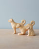 The Handmade Wooden Dog Family includes three small wooden dog figures of varying sizes, each with curled tails and simple facial features, displayed on a light wooden surface against a pale blue background.