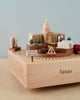 The Texas Wooden Music Box features a carved relief of Texas cultural landmarks and symbols, including structures like the state capitol, along with the engraved slogan "Don't mess with Texas.