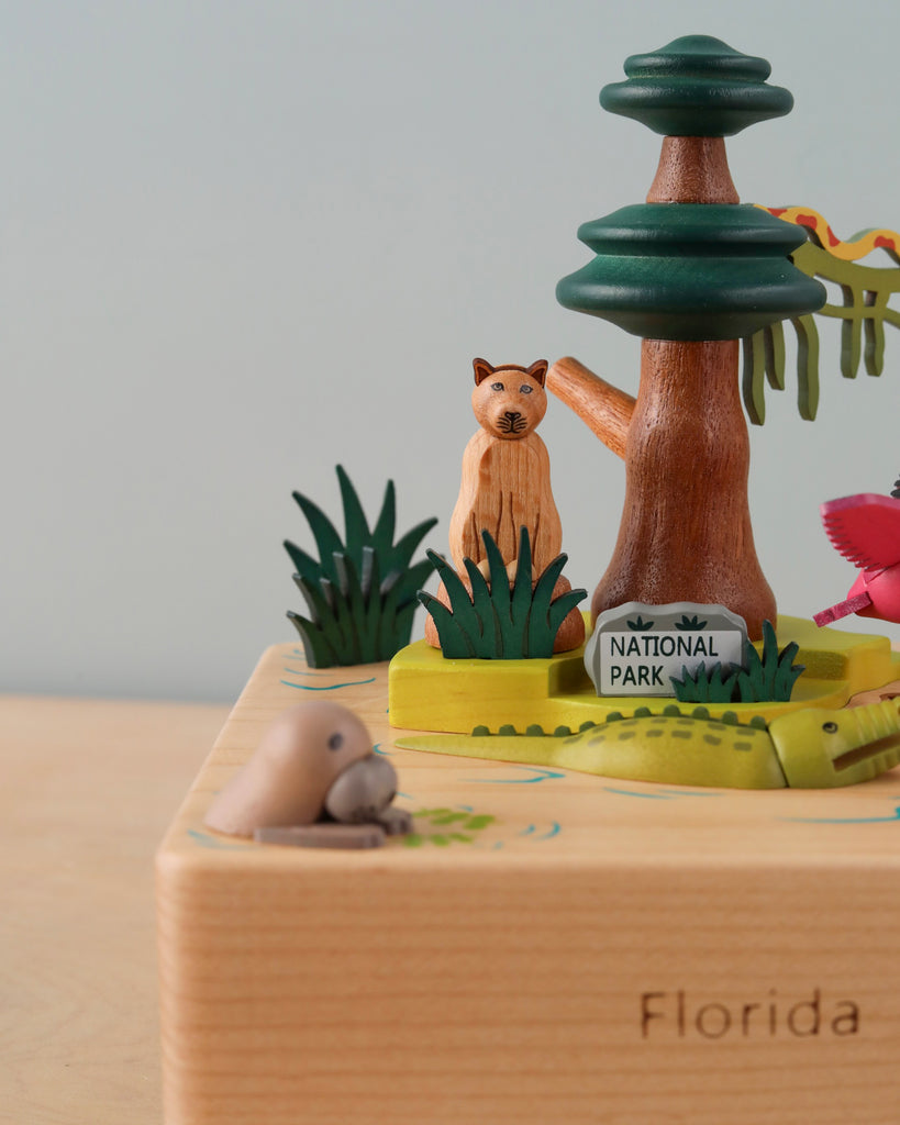 A colorful Florida Wooden Music Box featuring a Florida national park theme, with a sculpted cat, bird, manatee, and tree on a labeled base.