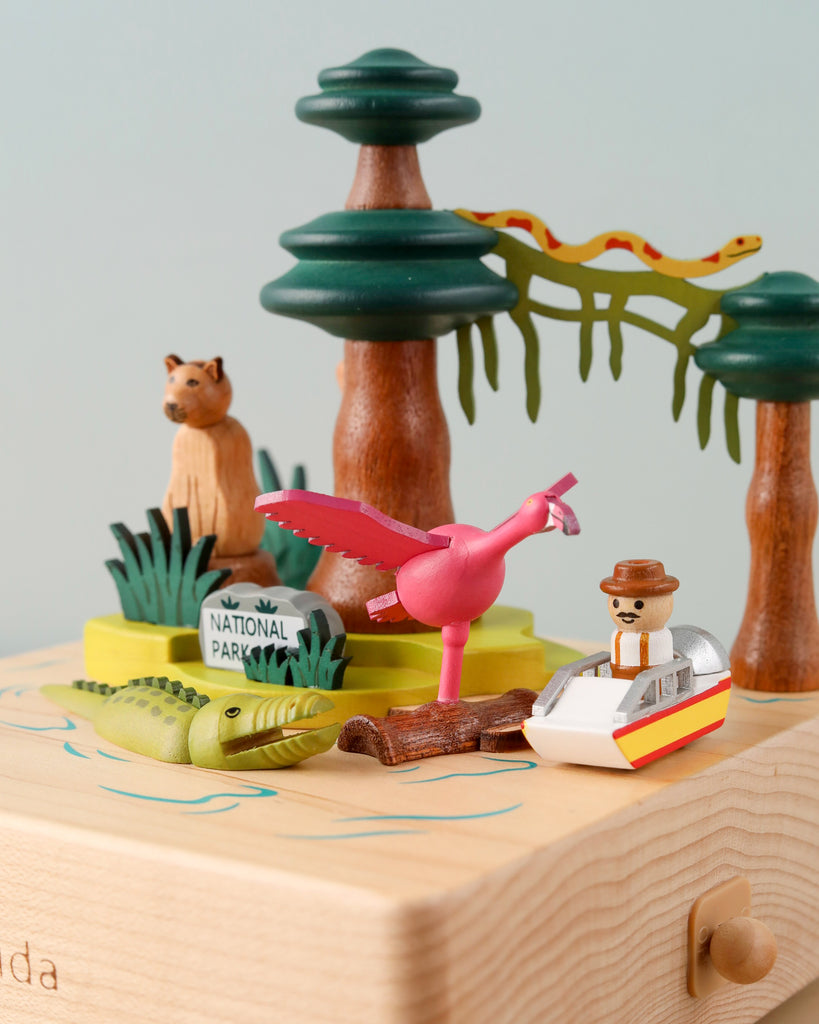 A colorful pop-up book featuring a 3D scene with wooden figures: an adventurer in a boat, a flamingo, crocodile, and a tree with a leopard, including a Florida Wooden Music Box.