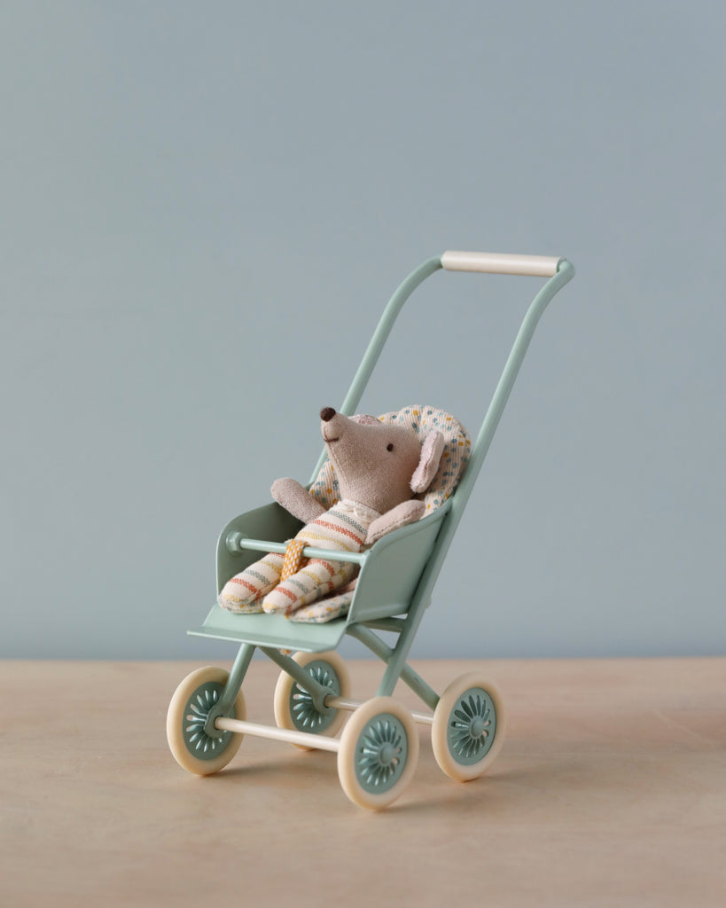 A plush toy mouse dressed in striped clothes sits in a Maileg Miniature Stroller, Micro - Mint against a plain, light blue background.