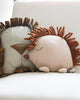 Two striped fabric lion toys with playful manes cuddle on a white couch, next to a Hedgehog Cushion, evoking a warm, cozy atmosphere.