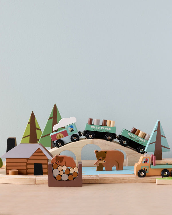 A playful Wild Pines Train Set featuring a train with cargo, trees, a house, and animal figures set against a neutral background.