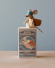 Sentence with product name: A Maileg | Superhero Mouse, Little Brother figurine dressed as a superhero with a cape, standing on top of a colorful matchbox labeled "Little Brother Superhero" against a light blue background.