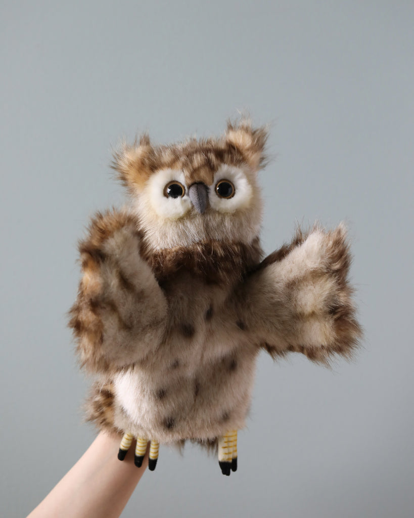 A Owl Puppet plush owl puppet is held up against a plain gray background, featuring large, expressive eyes and outstretched wings as if in mid-flight.