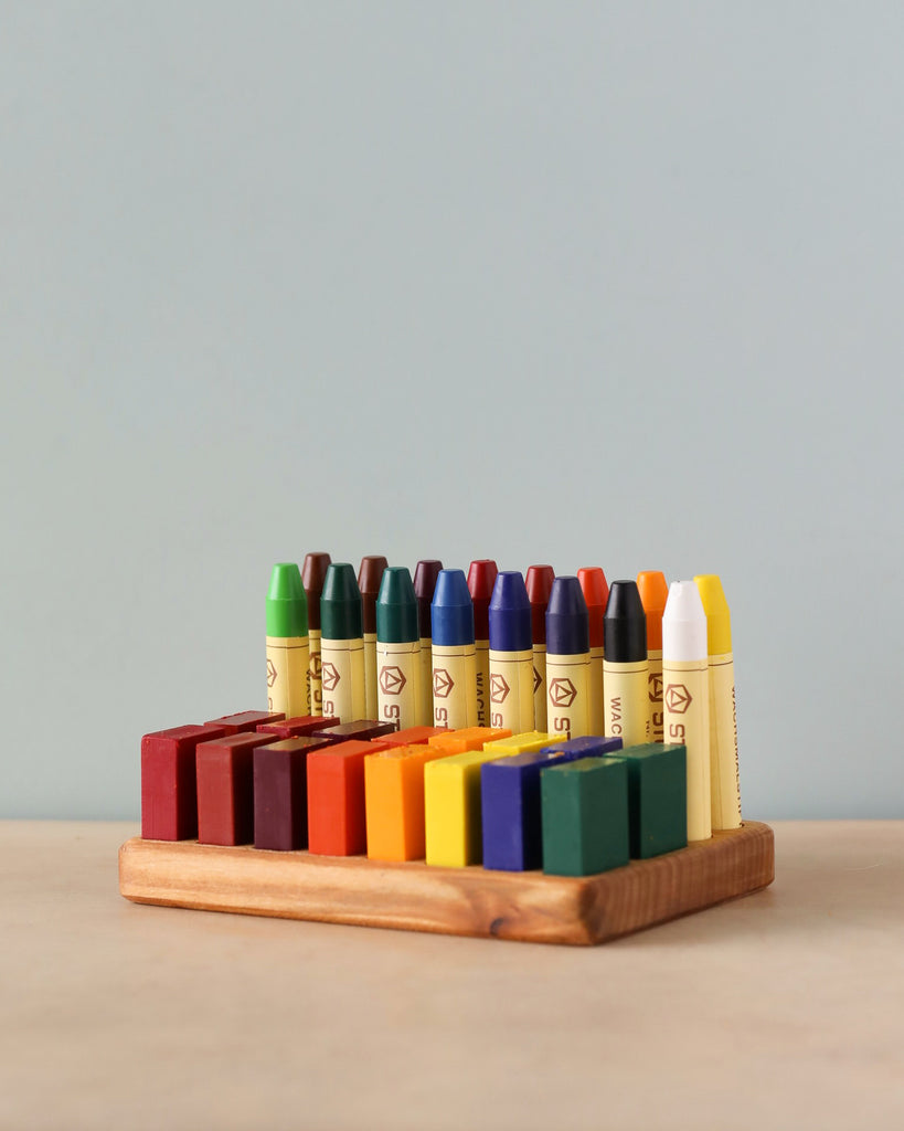 A Crayon Tray For Stockmar -16 x 16 Slots displaying a range of 16 different colored Stockmar sticks in a row against a soft grey background.