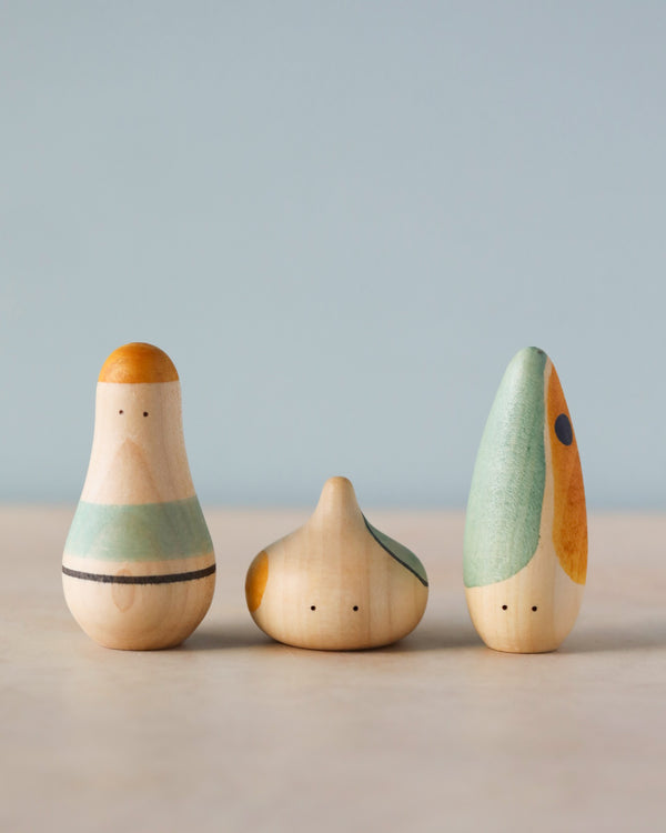 Three wooden Grapat Hooray! Play Sets with a simple, abstract design, painted in soft, earthy tones, stand against a plain, light blue background.