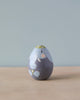 A Hand Painted Hollow Wooden Easter Egg - Elephant stands on a wooden surface against a light blue background. The design features soft gray colors with yellow accents on the top.