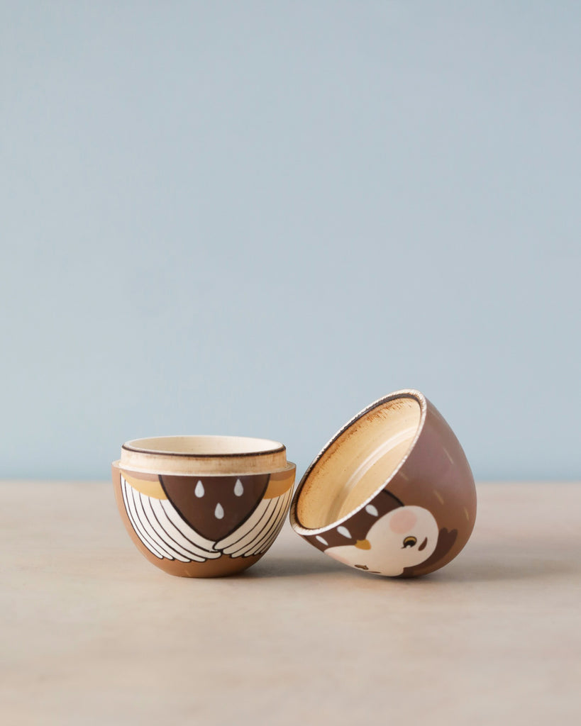 Two small handcrafted ceramic bowls with decorative patterns, one upright and the other tilted, on a Hand Painted Hollow Wooden Easter Egg - Owl against a pale blue background.