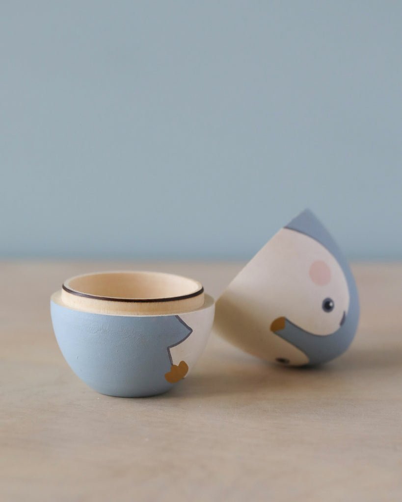 Two whimsical, handcrafted ceramic bowls painted to resemble Hand Painted Hollow Wooden Easter Eggs - Penguins, one upright and one tilted on its side, against a soft blue background.