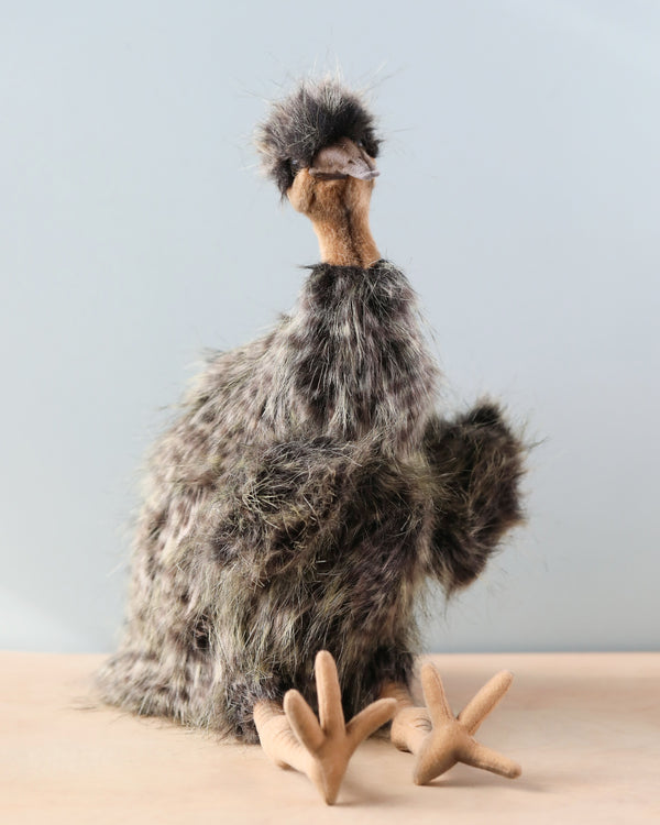 A quirky, handmade Emu Puppet resembling an ostrich, made from materials with various textures and colors. It features a long fuzzy neck, realistic features like big eyes, and flat felt feet, standing on.