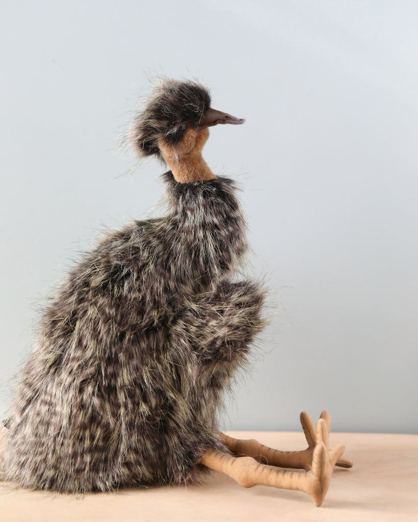 A Emu Puppet resembling a bird with realistic features, a fluffy body, long neck, and fur-like texture, sitting on a wooden surface against a light background.