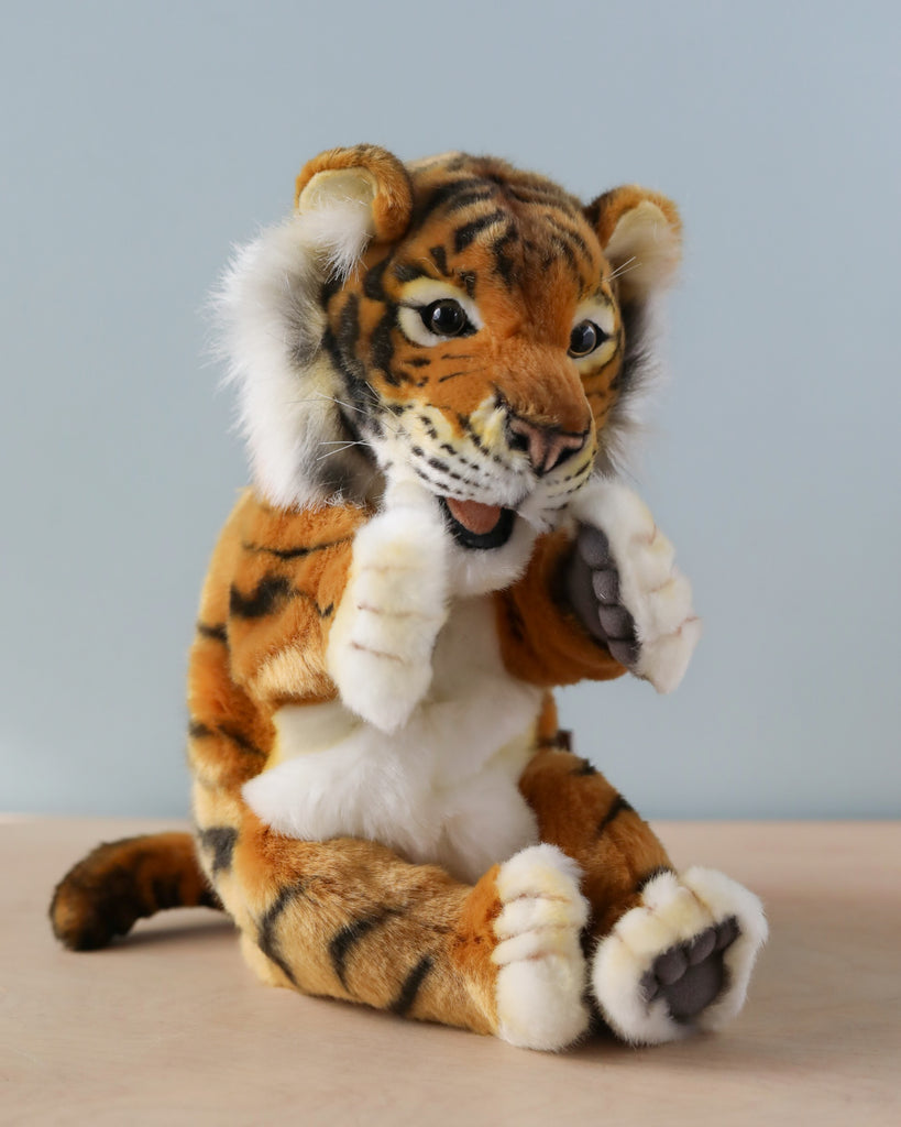 A Tiger Puppet with realistic details sits against a plain backdrop, featuring black stripes, a soft white belly, expressive eyes, and paws raised as if in mid-gesture.