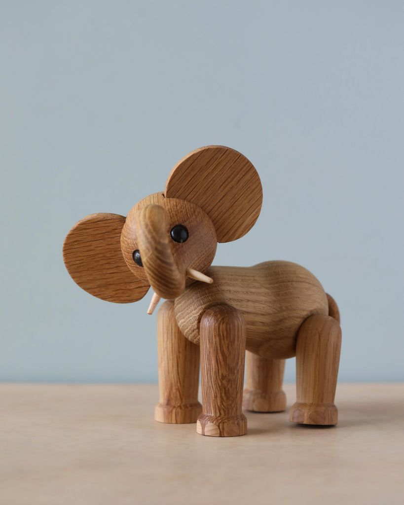 A Spring Copenhagen Ollie - Elephant toy crafted from FSC Oak with large round ears and tusks, standing against a light blue background.