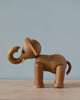 Spring Copenhagen Ollie - Elephant figurine crafted from FSC Oak, with a raised trunk and visible grain patterns, set against a light blue background. It features a small, carved tail and distinct eyes.