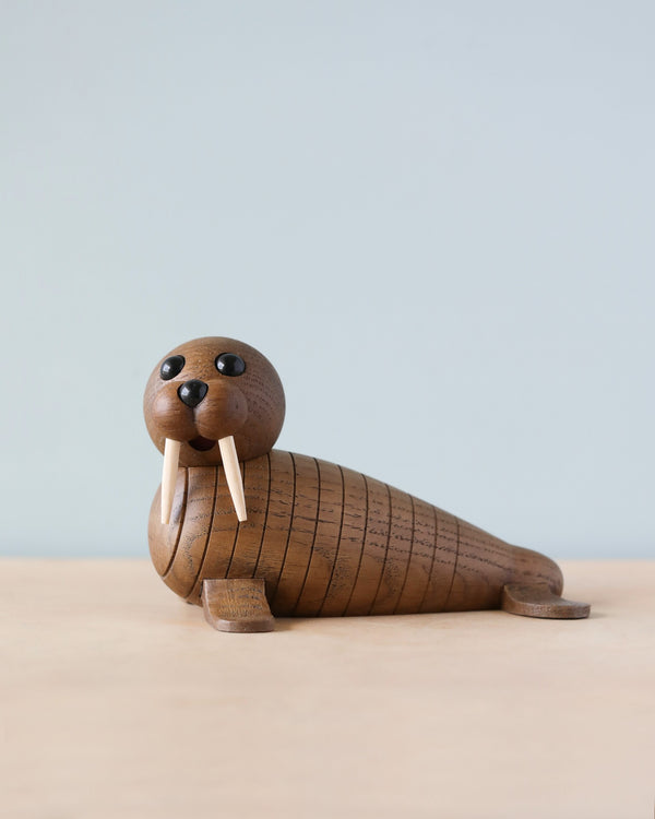 A Spring Copenhagen Wally sculpture with articulated segments and prominent eyes, featuring small stick-like teeth, positioned against a soft blue and beige background. This handmade wooden product captures the charming essence of nature's design.