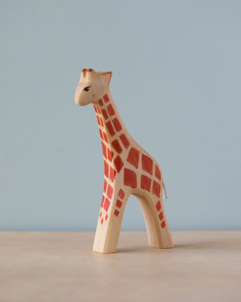 A Handmade Holzwald Giraffe - Large on a plain blue background, showcasing detailed red and brown spots and a small tail. This piece is part of our collection of sustainable wooden toys.