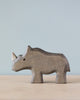 A Handmade Holzwald Rhino figurine standing against a soft blue background, showcasing a simple and smooth texture and design of high-quality wooden toys.