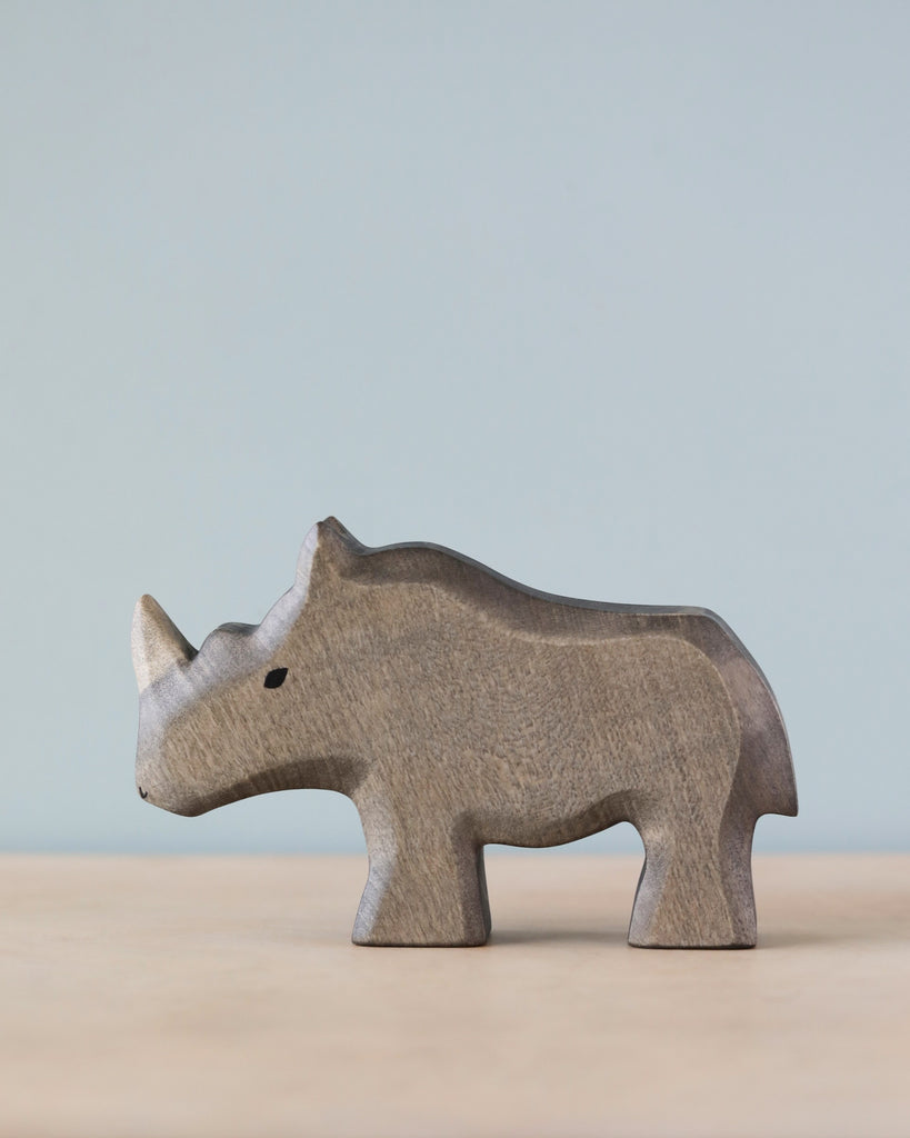 A Handmade Holzwald Rhino figurine standing against a soft blue background, showcasing a simple and smooth texture and design of high-quality wooden toys.