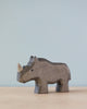 A Handmade Holzwald Rhino figurine, a sustainable toy, set against a soft blue background, showcasing detailed carving and a smooth, dark finish.