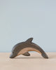A high-quality Handmade Holzwald Dolphin figurine is elegantly displayed against a soft blue background, capturing the essence of the creature with smooth, flowing lines and natural wood grain texture.