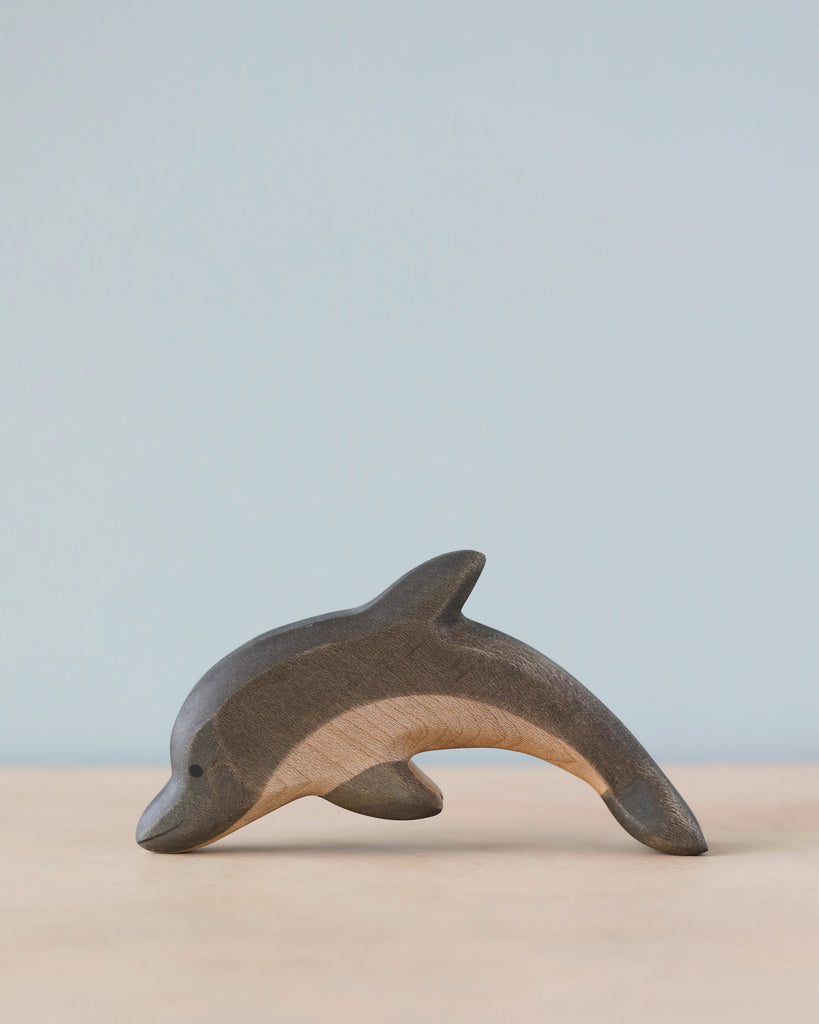 A high-quality Handmade Holzwald Dolphin figurine is elegantly displayed against a soft blue background, capturing the essence of the creature with smooth, flowing lines and natural wood grain texture.