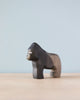 A Handmade Holzwald Gorilla figurine, crafted as a sustainable toy, stands on a light table with a plain blue background, displaying detailed carving and a dark finish.