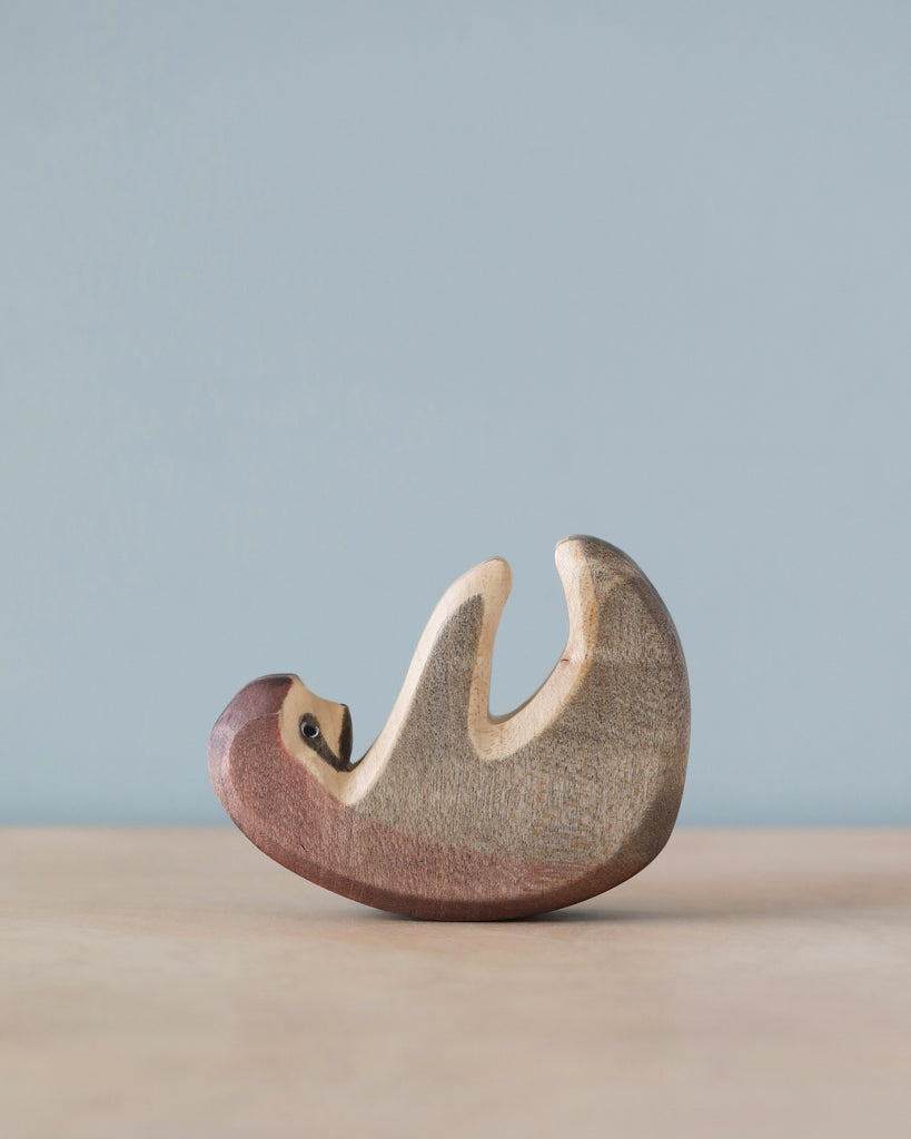 A high-quality Handmade Holzwald Sloth figurine resembling a sleeping fox with smooth contours and a minimalistic design, placed against a soft blue background.