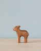 A small Handmade Holzwald Standing Fawn figurine with white spots on its side stands against a soft blue background. The fawn appears handcrafted and simple in design, embodying the qualities of sustainable toys.