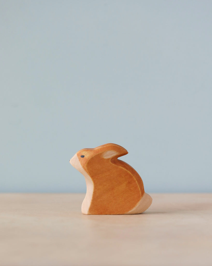 A small high-quality Handmade Holzwald Sitting Rabbit figurine sits on a smooth surface against a soft blue background, portraying a simple and minimalist aesthetic.